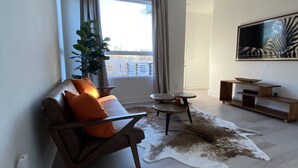 A modern living room with a sofa, a coffee table, a TV, and a large window with curtains. - 5 Queen Bed 4 Full Bath Luxury Home, 1.4 miles to Bank of America Stadium (Charlotte)