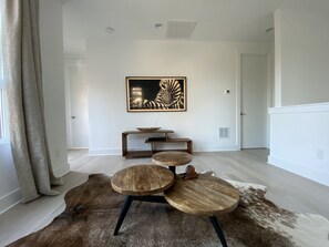 Una sala de estar moderna con una mesa de centro redonda de madera, una mesita auxiliar con un cuenco, y una obra de arte enmarcada en la pared.