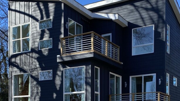 A modern two-story house with a dark exterior, multiple windows, and a wooden balcony. - 5 Queen Bed 4 Full Bath Luxury Home, 1.4 miles to Bank of America Stadium (Charlotte)