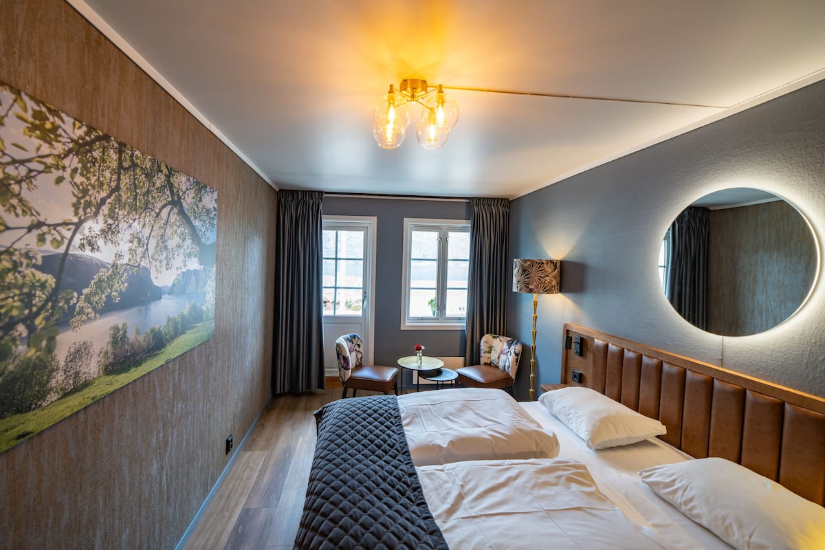 Ein Hotelzimmer mit einem Bett, einem Schreibtisch, einem Sessel, einer Lampe, einem runden Spiegel und einem Bild an der Wand.
