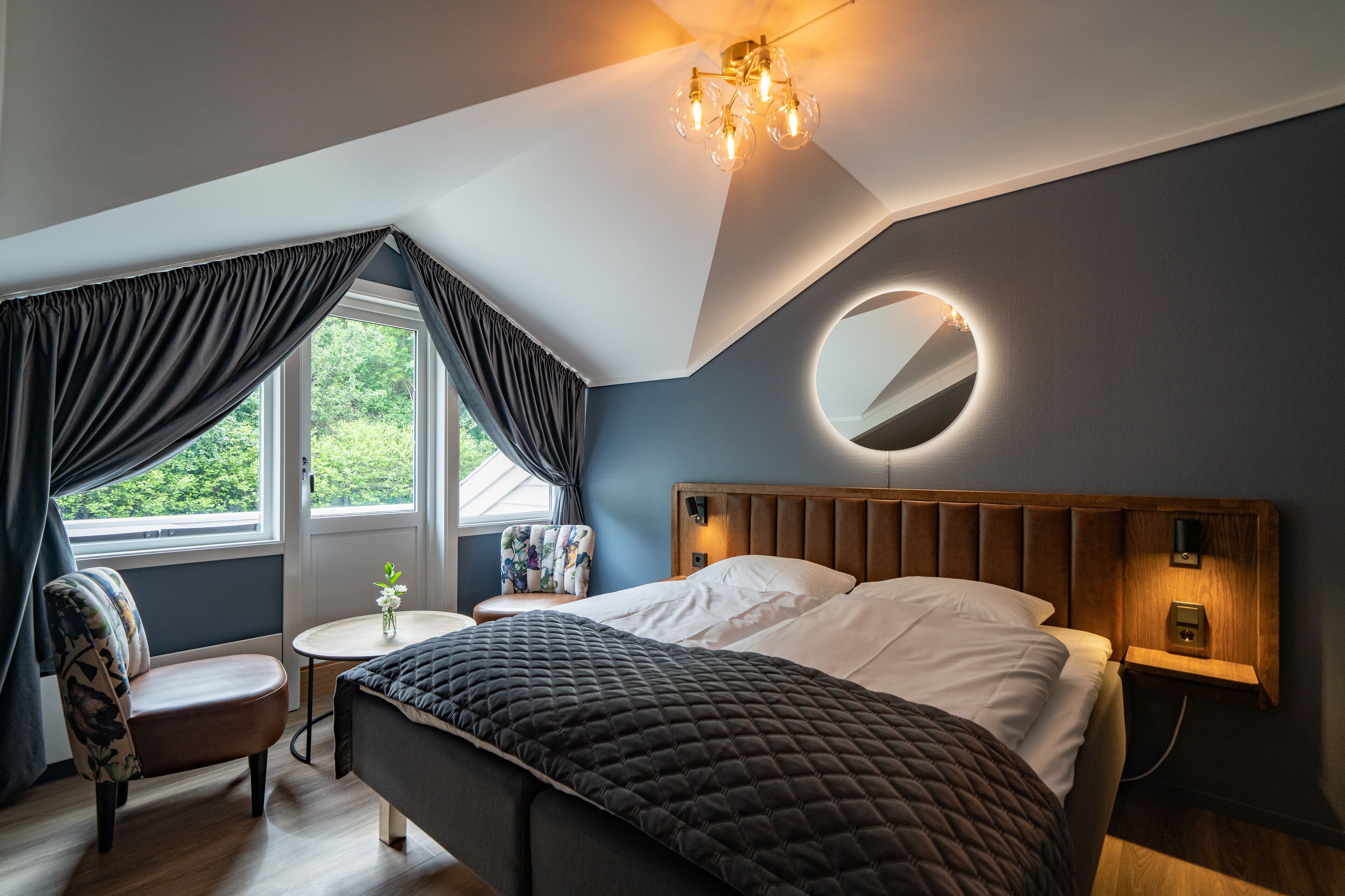 A modern bedroom with a large bed, a round mirror, a small round table, and a chair.
