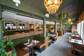 Ein Restaurant mit Sitzboxen, hängenden Pflanzen und Pendelleuchten.