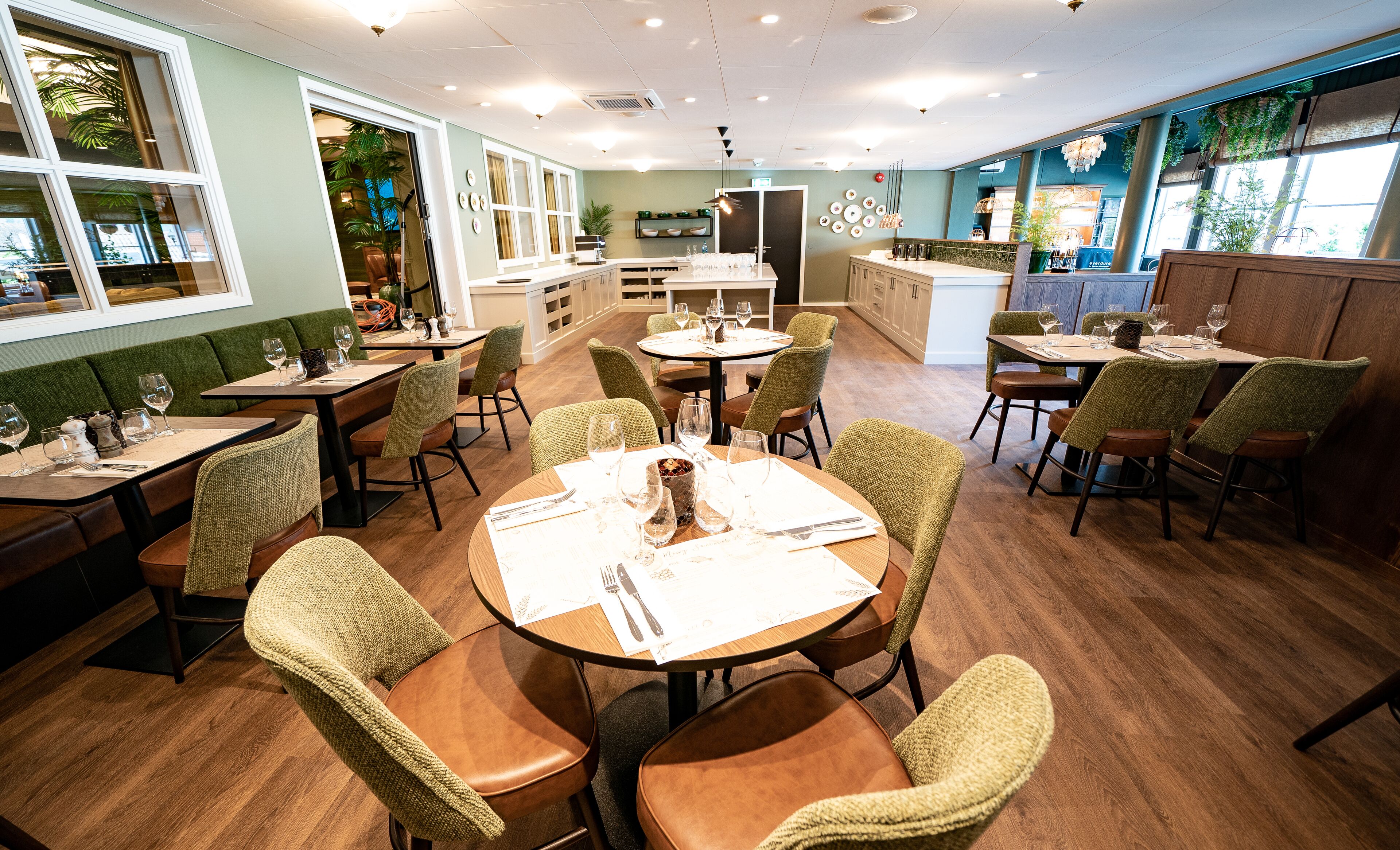 Un restaurante con mesas redondas, sillas tapizadas de verde y suelo de madera.