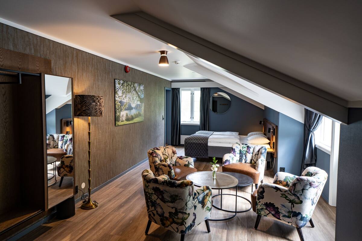 Ein modernes Schlafzimmer im Loftsstil mit schrägen Wänden, einem großen Bett, einer Sitzecke mit Sofa und Sesseln sowie einem Esstisch.