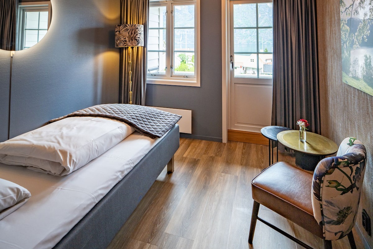 Ein modernes Schlafzimmer mit einem Bett, einem Sessel, einem runden Tisch und einem Fenster mit Vorhängen.
