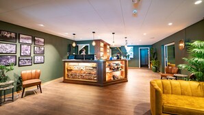 Un hall con mostrador de recepción de madera, sillones de cuero y un sofá amarillo.