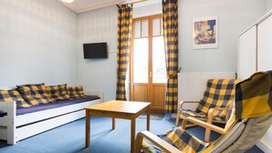 Ein Zimmer mit einer Couch, einem Holztisch, einem Stuhl und einem Fenster mit Vorhängen.