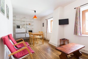 Une pièce de taille modeste, avec une table à manger en bois, un téléviseur fixé au mur et une fenêtre agrémentée de rideaux.
