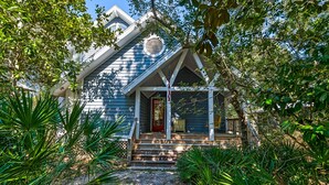 A house with a steeply pitched roof, a front porch with steps, and a red door.