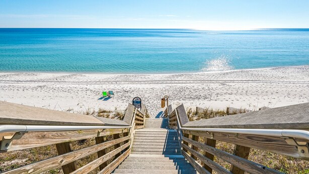 A wooden staircase leading to a beach with a clear view of the ocean.