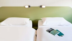 Une chambre d’hôtel avec deux lits, du linge de lit blanc, une tête de lit verte et un luminaire fixé au mur.