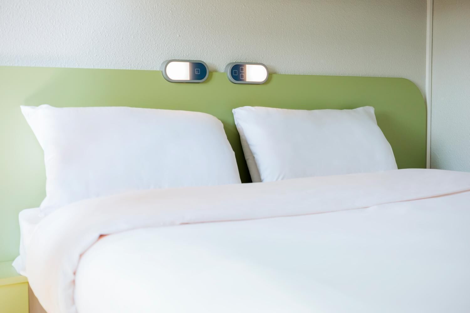 A bed with white bedding and a green headboard.