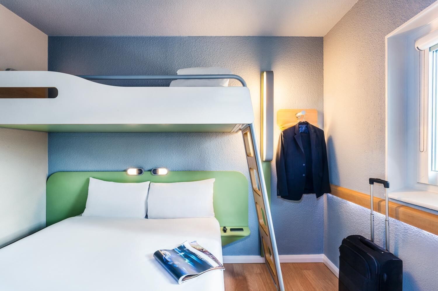 A bunk bed room with a magazine on the bed, a suitcase, and a jacket hanging on the wall.
