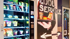 Un distributeur automatique de collations et de boissons, une pancarte indiquant « SERVICE RAPIDE » et une main tenant une tasse de café.