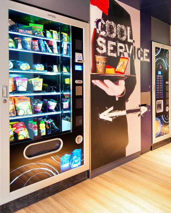 Un distributeur automatique de collations et de boissons, une pancarte indiquant « SERVICE RAPIDE » et une main tenant une tasse de café.
