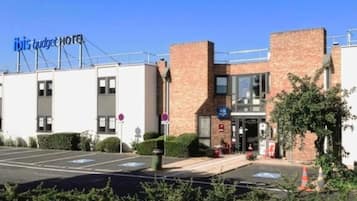 Een hotel met een bord waarop 'ibis budget hotel' staat, een parkeerplaats met aanduidingen en een gevel van baksteen.