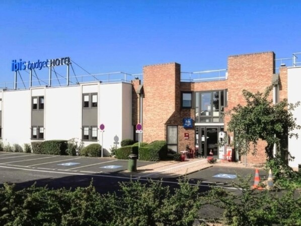 A hotel with a sign reading 'ibis budget hotel,' a parking lot with marked spaces, and a brick building facade. - ibis budget Clermont-Ferrand Le Brézet Aéroport (Clermont-Ferrand)