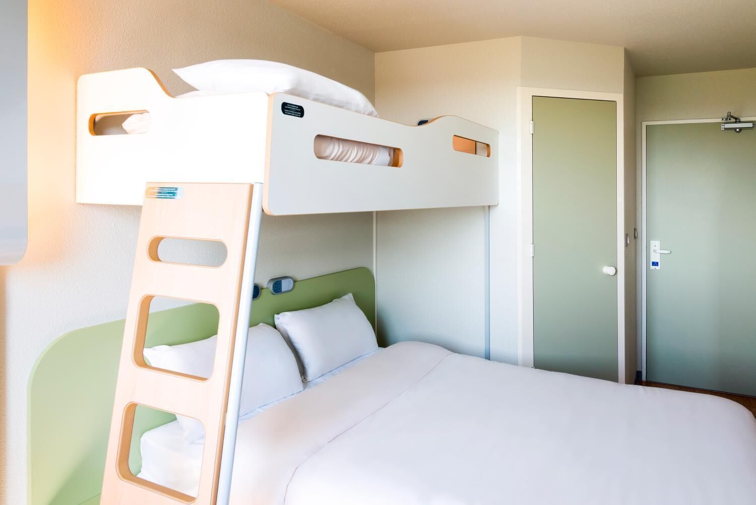 Een stapelbed met een ladder, een enkel bed beneden, en een deur aan de rechterkant.
