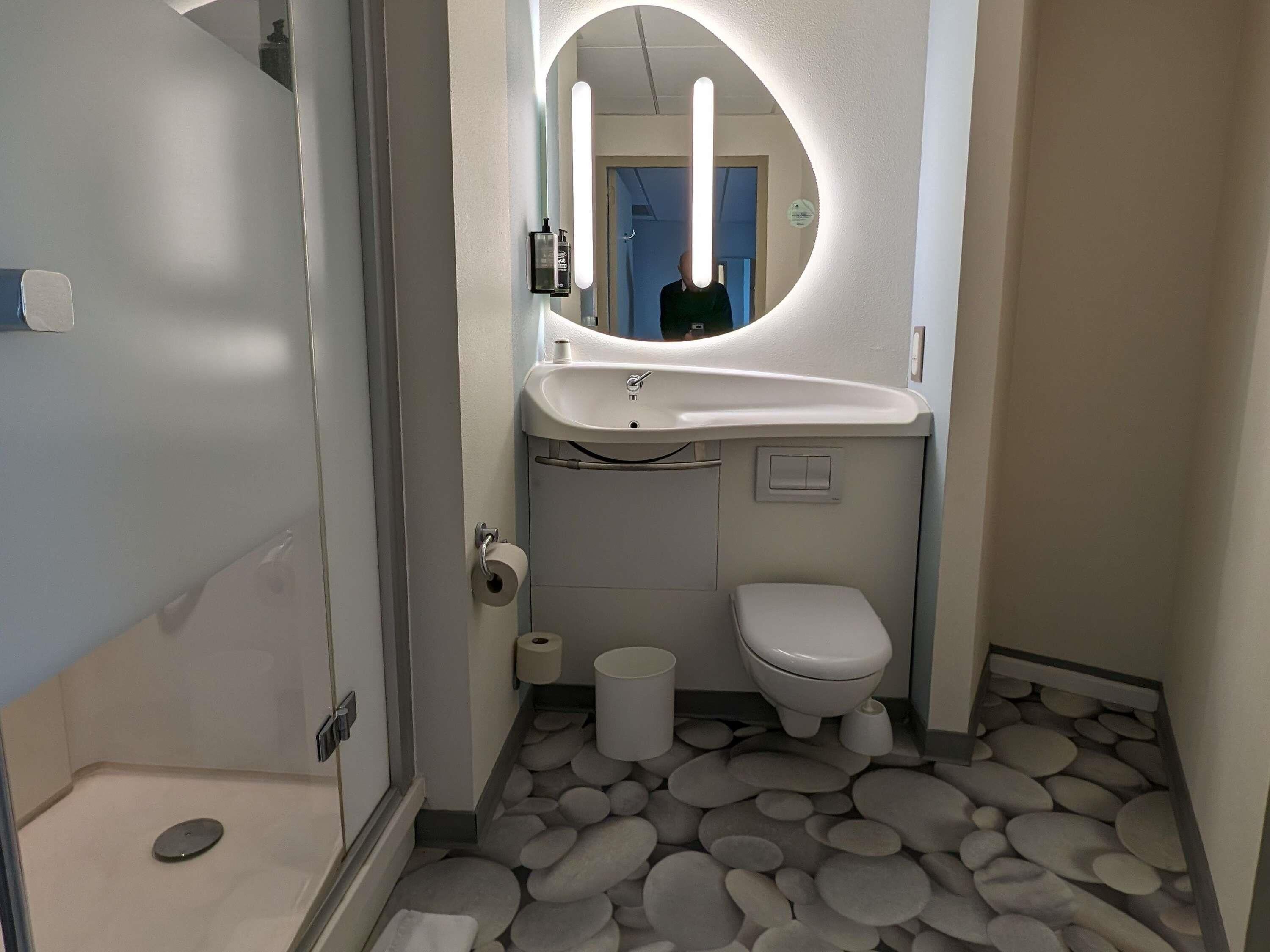 Une petite salle de bain comprenant un lavabo, des toilettes et un miroir avec un éclairage circulaire.