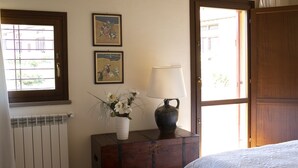Ein Zimmer mit einem hölzernen Schminktisch, einer weißen Heizung, zwei gerahmten Bildern, einer Blumenvase, einer Lampe und einem Bett.