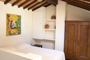 A bedroom with a bed, a wooden wardrobe, a white cabinet, and a colorful painting on the wall.