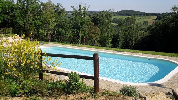 Ein Schwimmbecken mit Holzzaun, umgeben von Grün und Hügeln im Hintergrund.