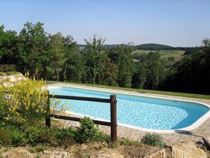 A swimming pool with a wooden fence, surrounded by greenery and hills in the background.
