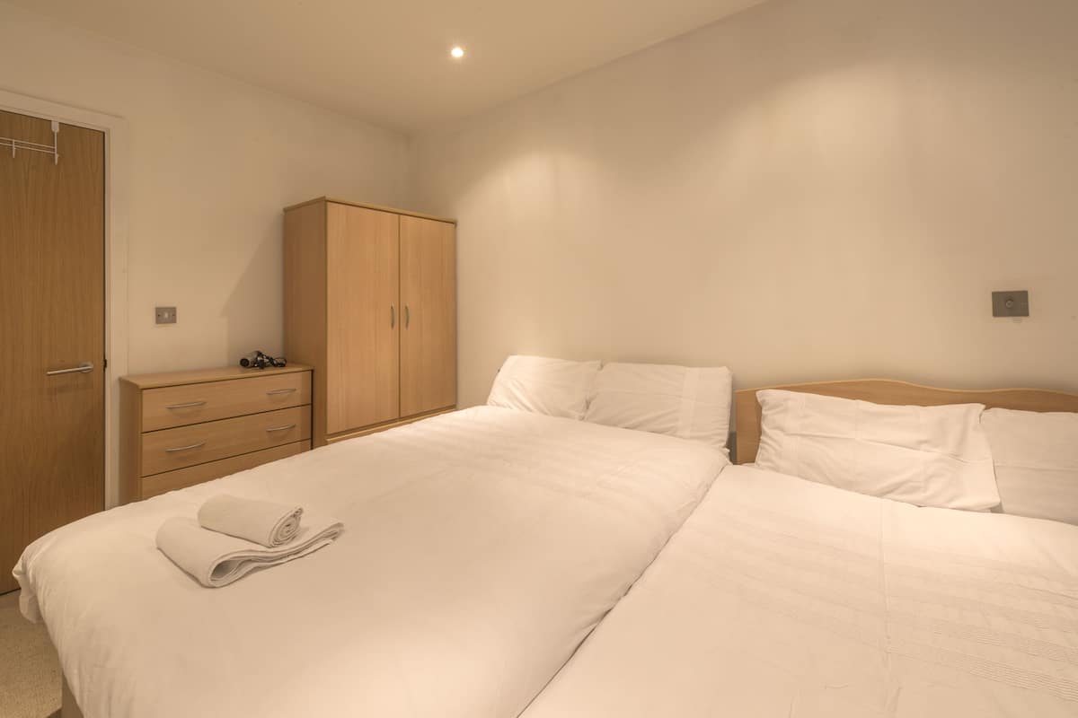 Quarto com uma cama grande, um guarda-roupa de madeira e uma mesa de cabeceira com abajur.