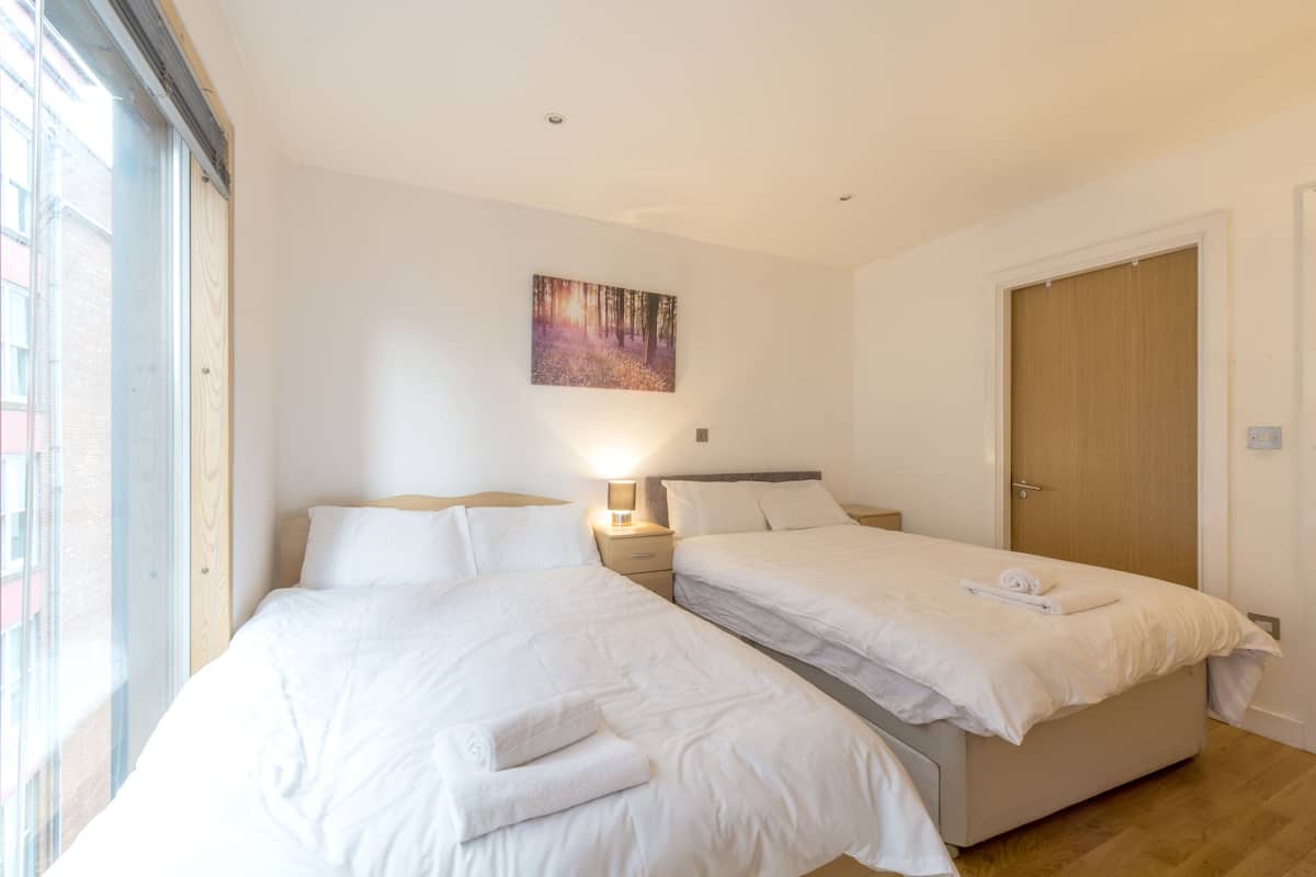 Quarto de hotel com duas camas, uma porta de madeira e um quadro na parede.