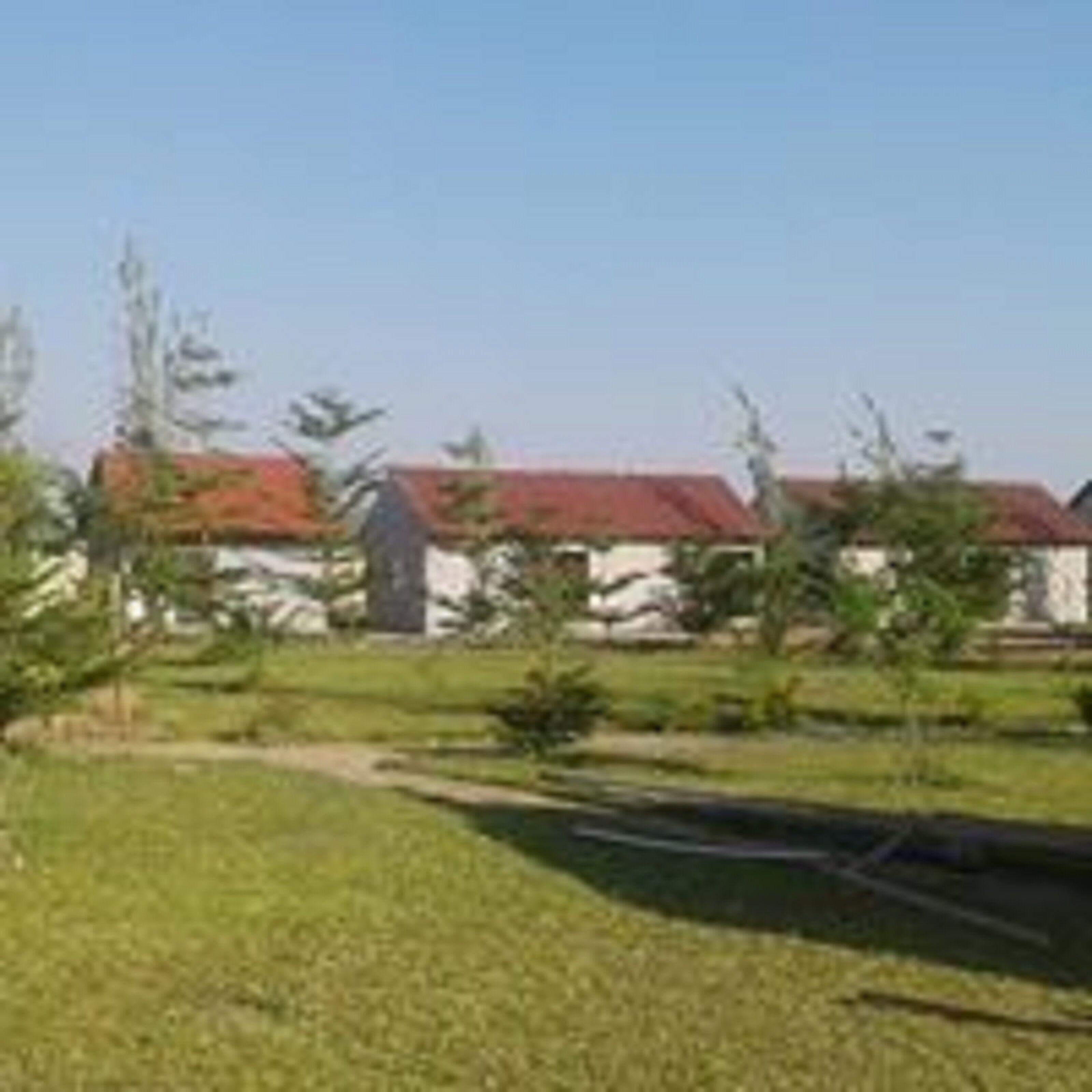 A building with a red roof, surrounded by a grassy area with trees and a clear sky.