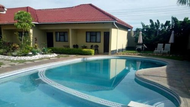 Une piscine à bords incurvés, une maison avec un toit rouge et un ciel bleu azur.