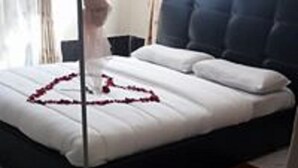 Un lit recouvert d’une courtepointe blanche et orné d’une décoration en forme de cœur, faite de pétales de rose.