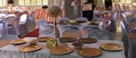 A banquet hall with tables set for a meal, chairs covered with white tablecloths, and a person standing in the background.