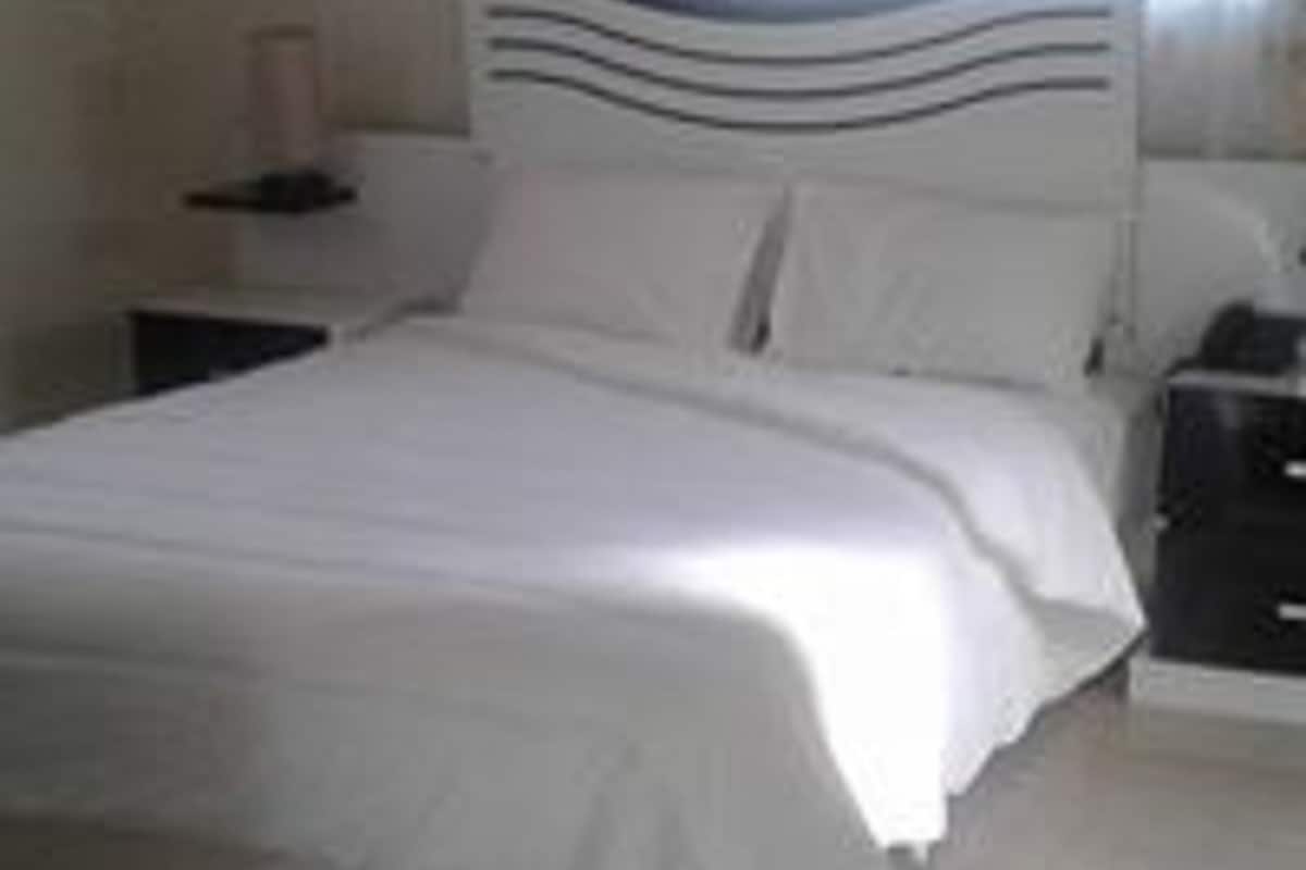 Cama bem arrumada em quarto com cabeceira branca e mesa de cabeceira.