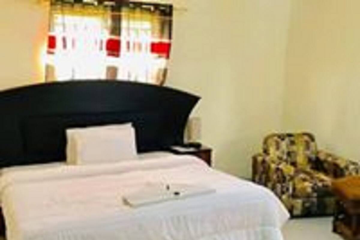 Uma cama bem arrumada com roupa de cama branca, cabeceira escura e mesa de cabeceira com abajur.