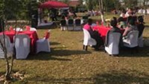 Un événement en plein air avec des tables rondes recouvertes de nappes blanches et rouges, entourées d’arbres et sous un ciel dégagé.