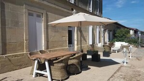 Ein Sitzbereich im Freien mit Tisch, Stühlen, einem großen Sonnenschirm und Blumentöpfen.