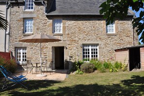 Un bâtiment en pierre doté d’un patio, d’un espace extérieur aménagé pour s’asseoir et d’une moto garée à l’intérieur.