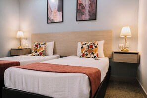 A hotel room with two single beds, each with a floral pillow and a bedside table with a lamp. - Casa Franco Hotel (Cartagena)