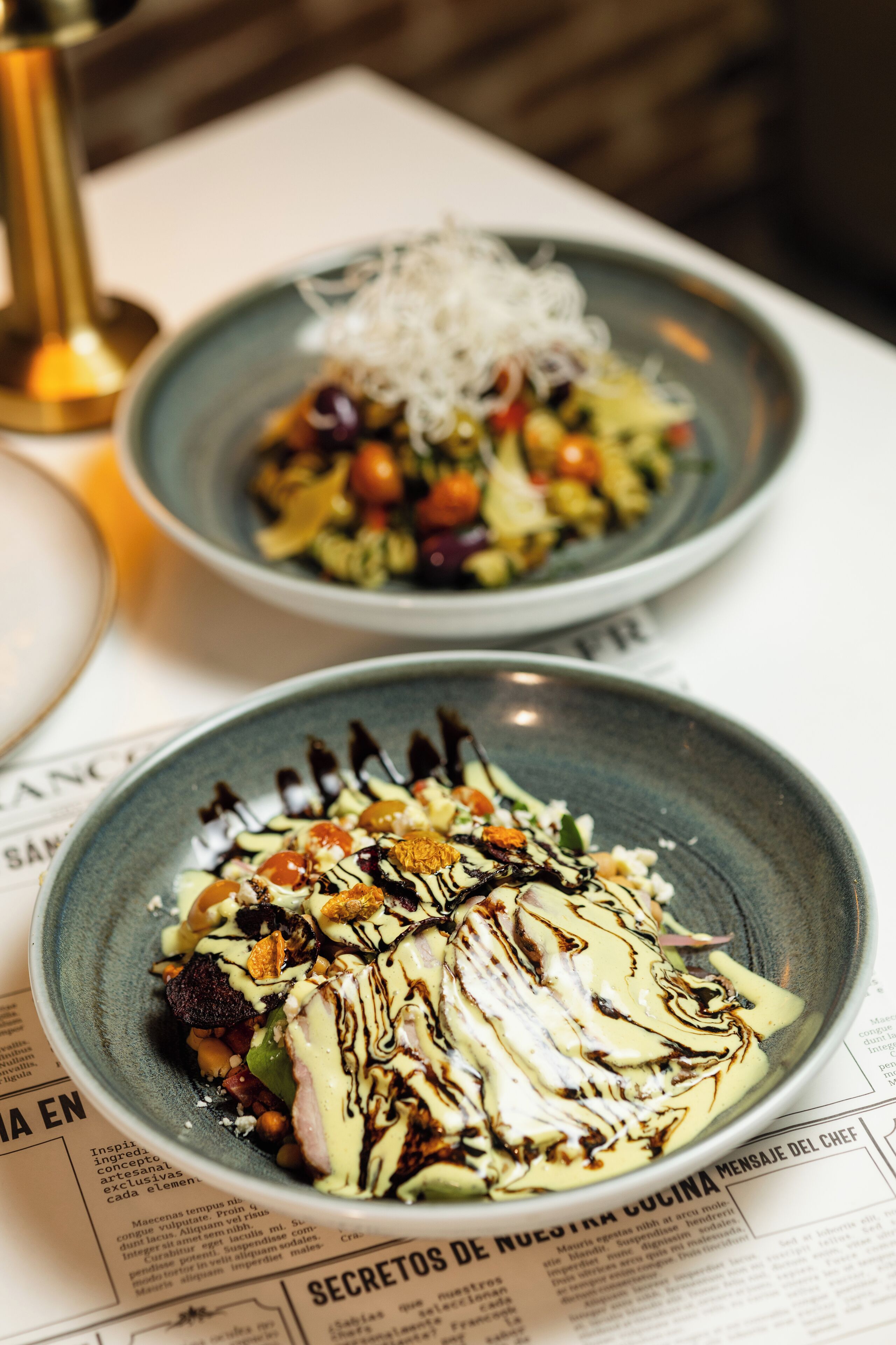 Two plates of food with a variety of ingredients and garnishes, placed on a table with a menu underneath.