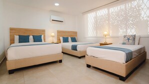 A hotel room with three beds, each with a wooden headboard, white bedding, and blue accents. There is a window with a lattice design, and an air conditioning unit mounted on the wall. - Casa Franco Hotel (Cartagena)