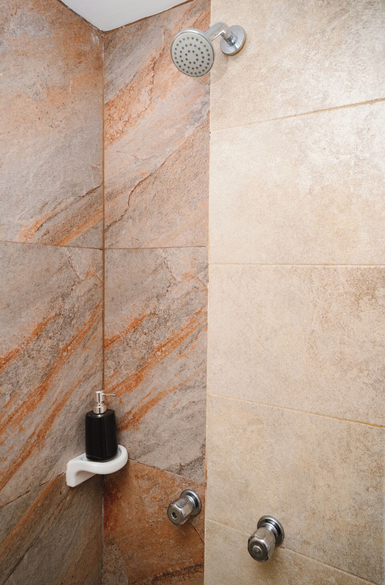 A bathroom with marble walls, a showerhead, a soap dispenser, and a towel rack.