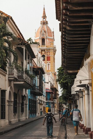 A narrow street with historic buildings, a prominent church with a dome, and pedestrians. - Casa Franco Hotel (Cartagena)