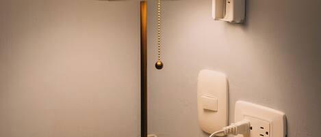 A bedside table with a lamp, a power outlet, and a wall socket.