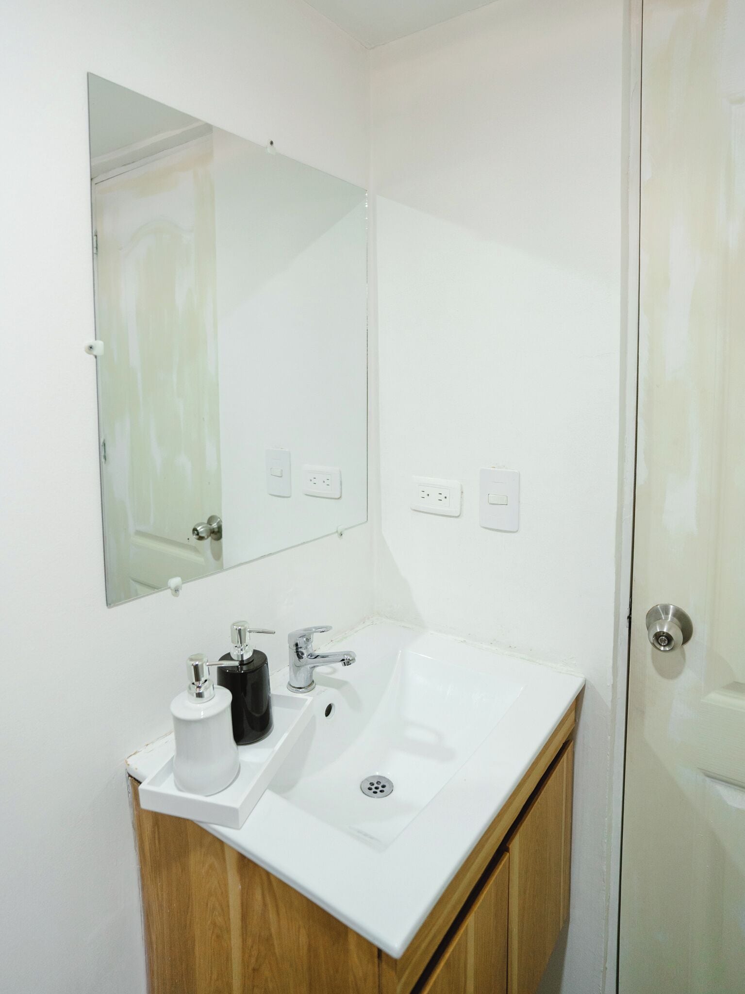A bathroom with a white sink, two faucets, a mirror, and a toilet paper holder.