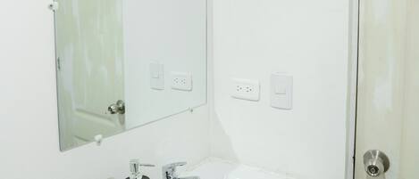 A bathroom with a white sink, two faucets, a mirror, and a toilet paper holder.