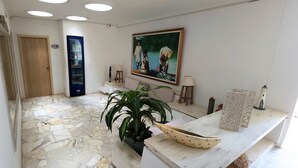 A reception area with a tiled floor, a wooden door, a refrigerator, a painting, a potted plant, and a decorative boat on a counter. - Casa Franco Hotel (Cartagena)