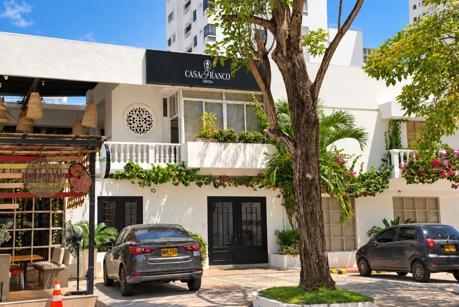A hotel with a black and white facade, outdoor seating, and a tree in the foreground.