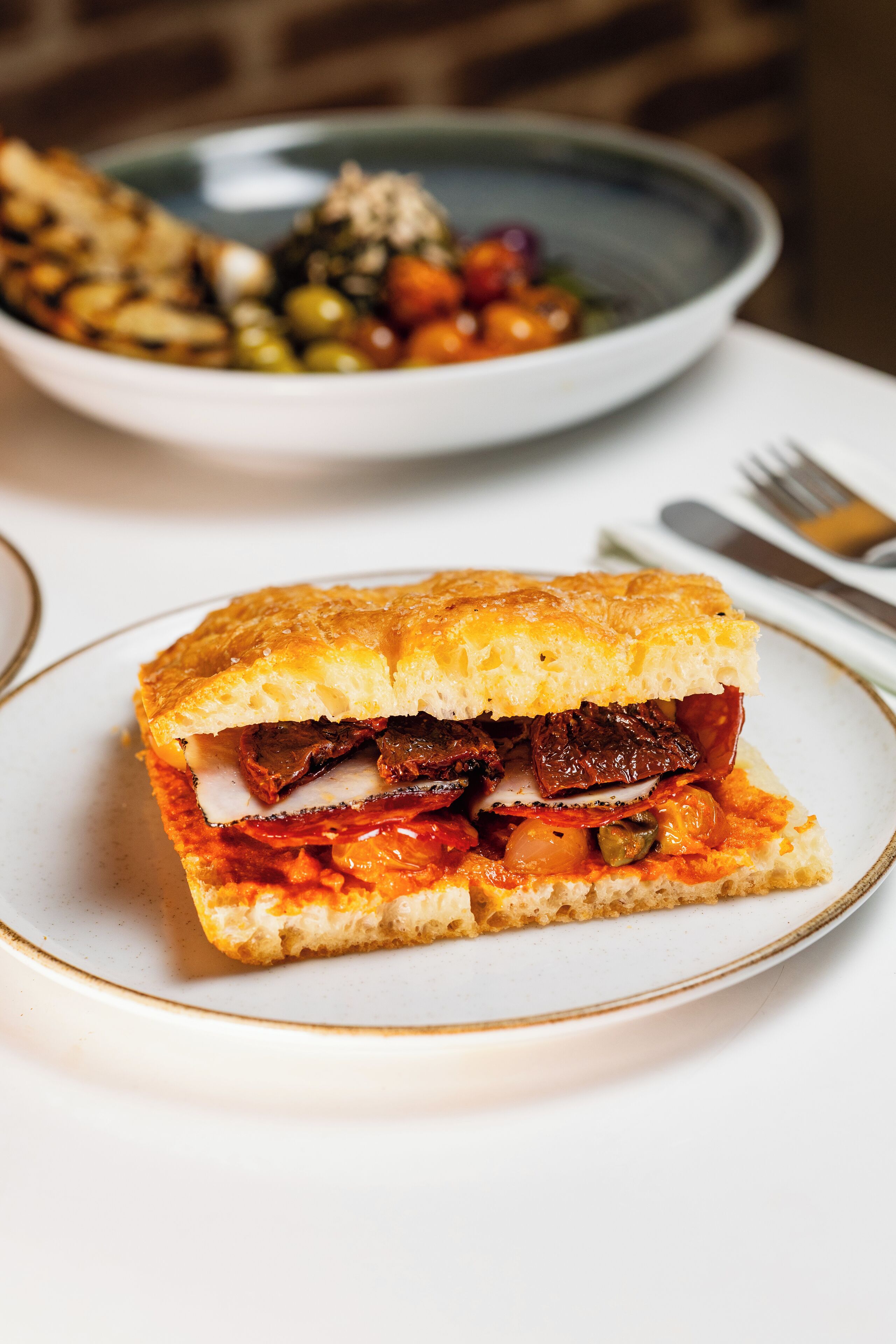 Un sándwich en un plato, con un tenedor y un cuchillo a un lado.