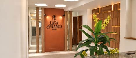 Un hall d'accueil d'hôtel avec une enseigne indiquant « HÔTEL CASA FRANCO » et un comptoir de réception agrémenté d'une plante.